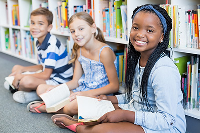 A boy and two girls holding books and smiling at the camera.